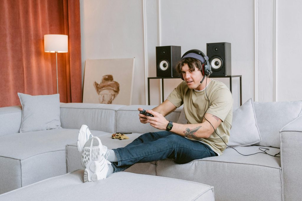 Young man sitting on a couch, enjoying video gaming at home with headphones on.